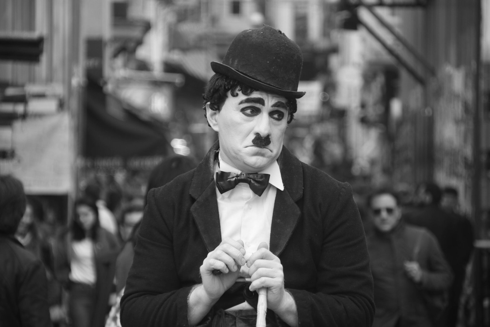 Black and white photo of a street performer dressed as a classic silent film character with a bowler hat.